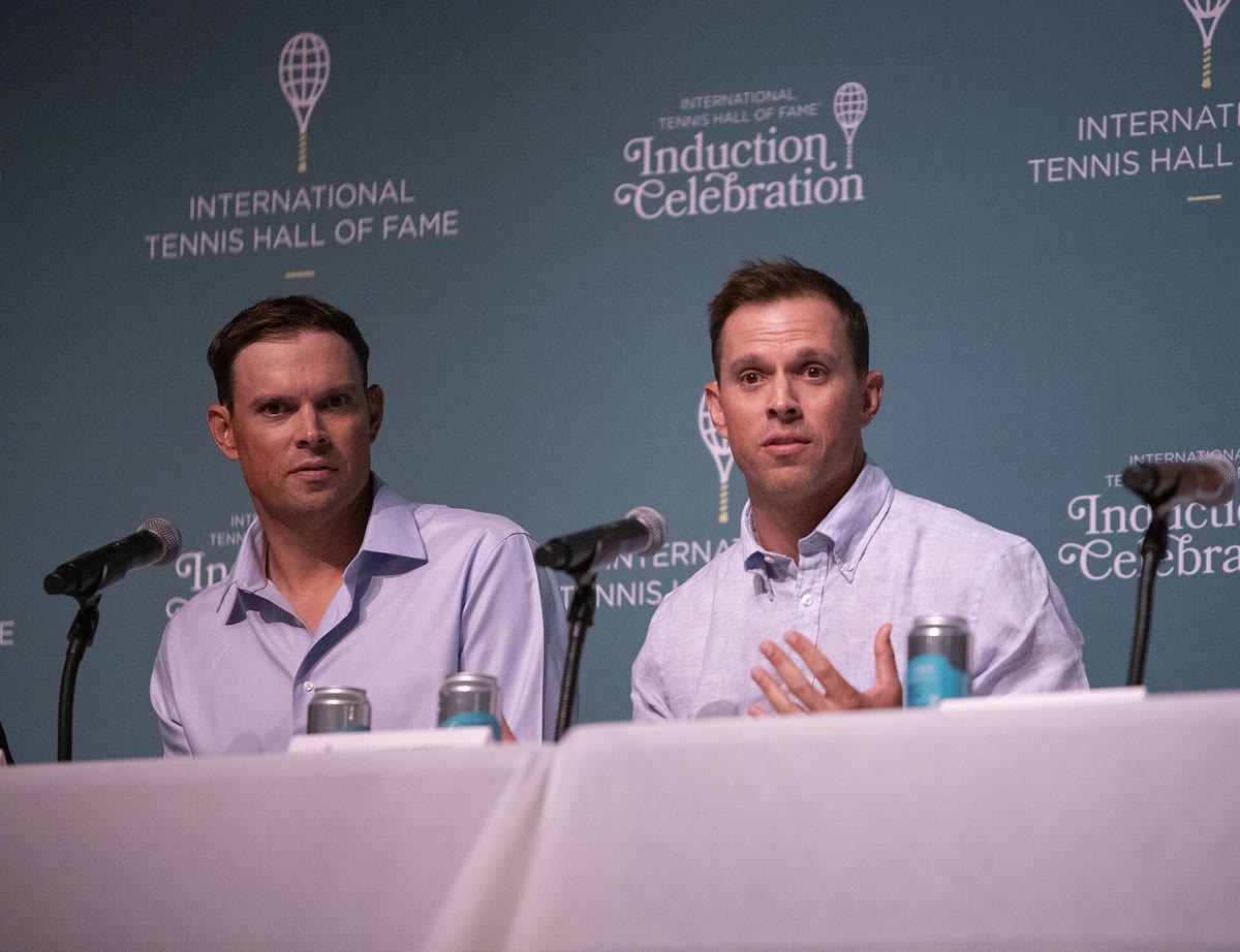 Bob and Mike Bryan at a press conference table in front of an International Tennis Hall of Fame backdrop.